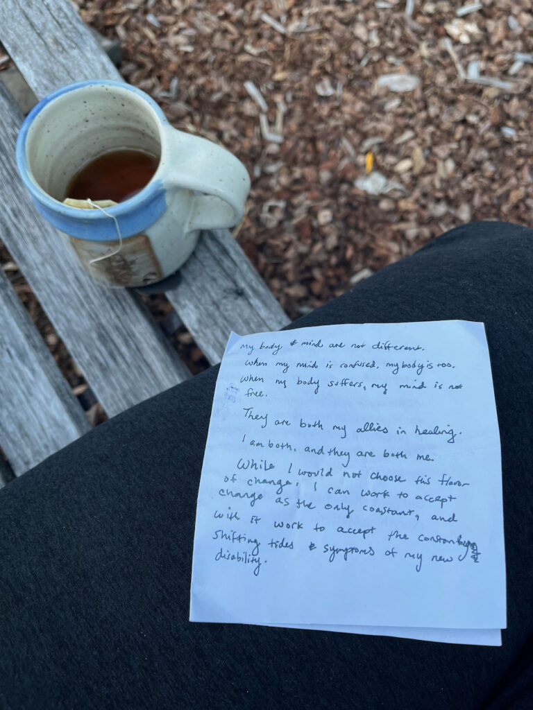 An image composed of angled pieces. the bottom angle is of woodchips and plant matter. the next layered angle is a bench with a hand-thrown ceramic mug on it. The final visible angle is my leg, on which a note rests. the note reads "my body & mind are not different. when my mind is confused, my body is too. when my body suffers, my mind is not free. They are both my allies in healing. I am both, and they are both me. While I would not chose the flavor of change, I can work to accept change and the only constant, and with it work to accept the constantly shifting tides & symptoms of my new disability.